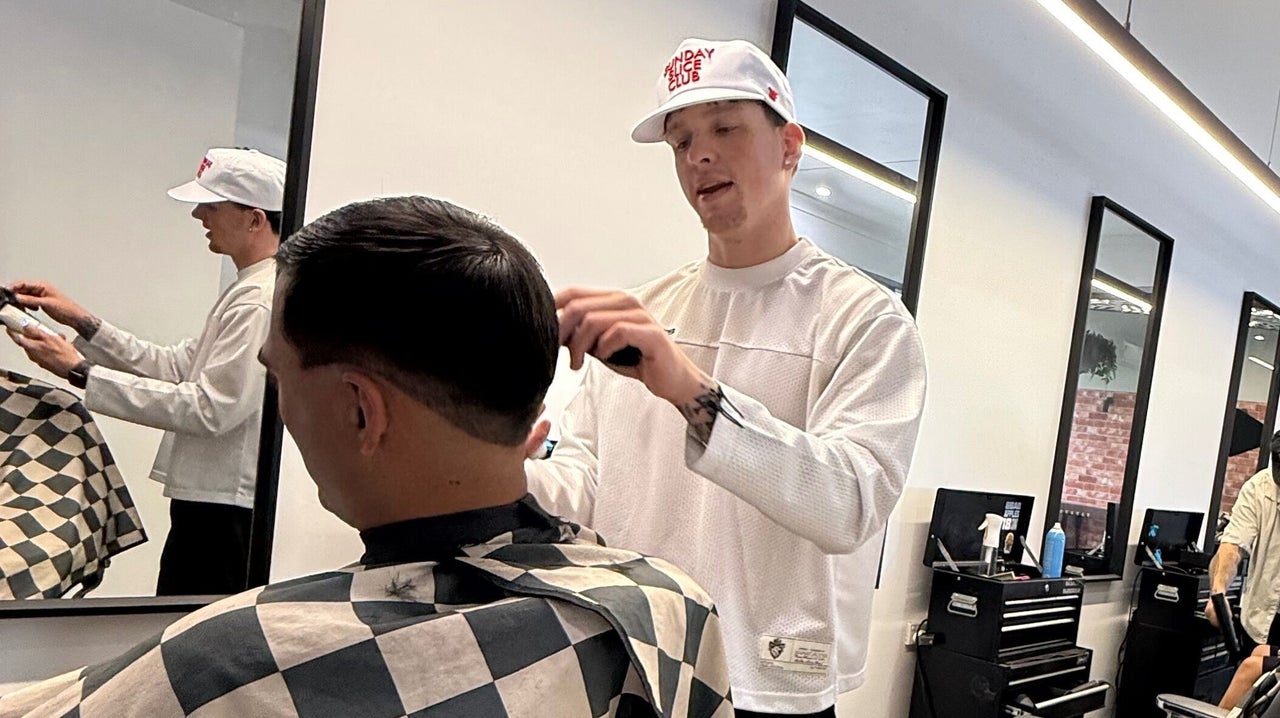 A Backbone barber in a white cap mid cut, checkered cape and mirrors behind