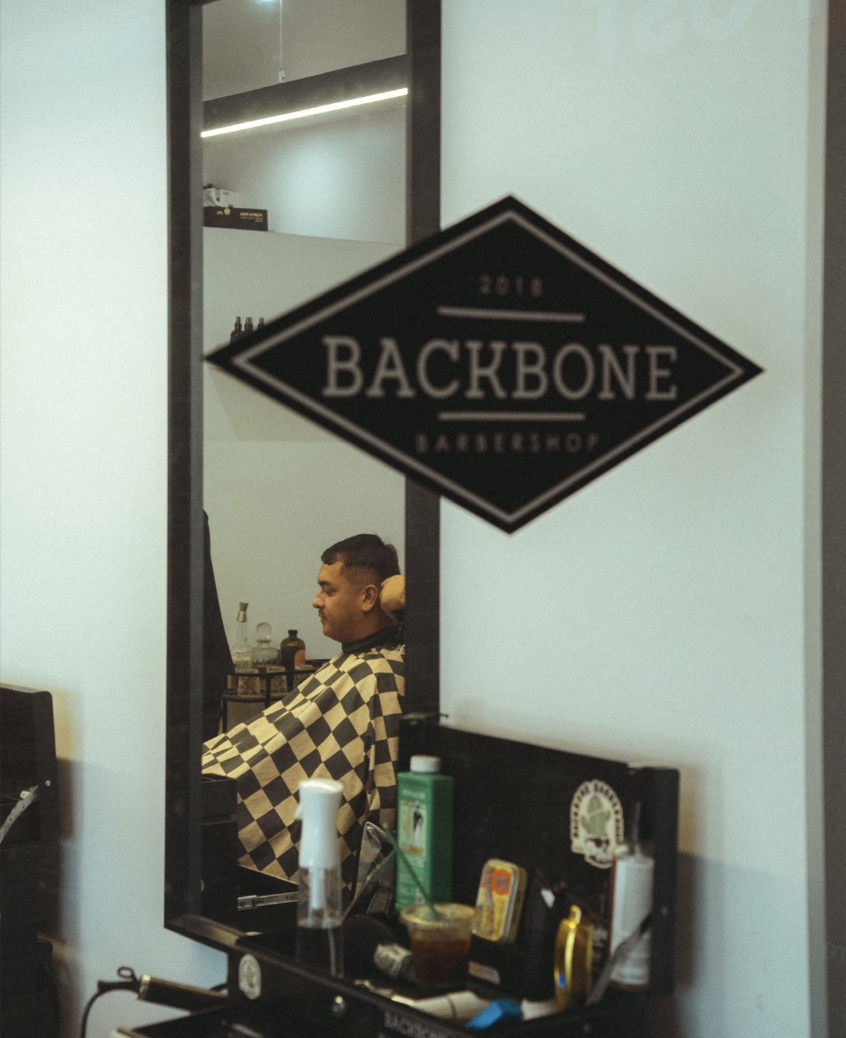 The Backbone diamond logo on the wall beside a barber station and mirror
